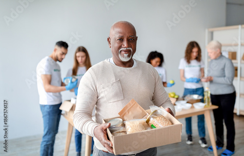 Photos An African American senior man smiles at the camera while holding a box of food donations
