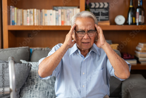 Wallpaper Mural Senior man holding his head in pain while sitting on couch at home. Elderly man suffering from headache, stress, or dizziness indoors. health care problem Torontodigital.ca