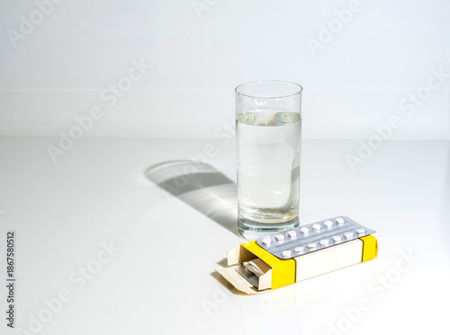 A box of pills and a glass of water on white glass, with shadow, copy space