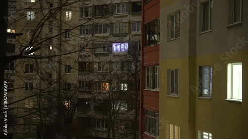 Quiet night scene of a vintage residential building with softly glowing windows, leafless trees framing the facade, capturing calm urban solitude under gentle night lighting
