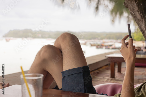 Valokuva Person lounging with legs up, using a smartphone near a waterfront cafe