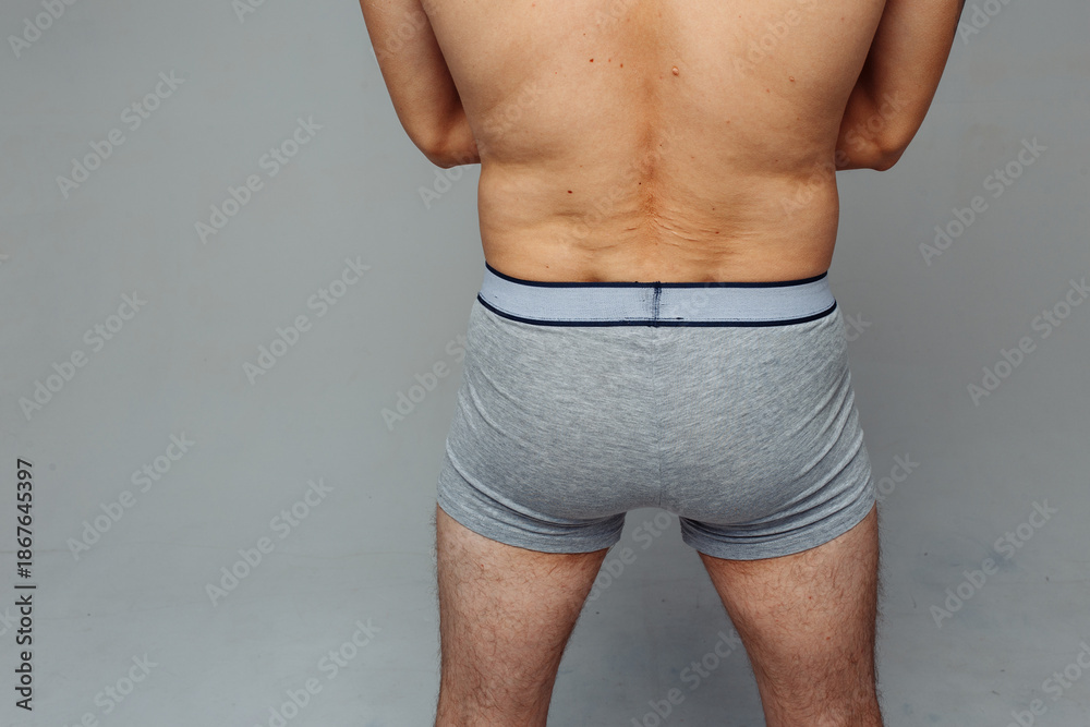Obraz premium firm male ass in gray briefs. man standing with his back to the camera in underwear. concept: male health. loose skin on the lower back after diets and stress.
