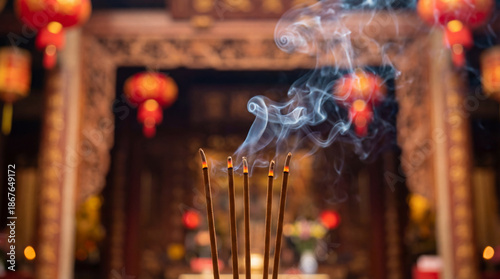 Burning incense sticks in temple. Incense smoke curls above incense during prayer ritual, warm lantern bokeh behind, for Chinese New Year celebration, Lunar New Year blessing, copy space