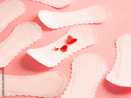Seamless pattern of white feminine sanitary pads with red paper hearts on pink background menstruation hygiene concept