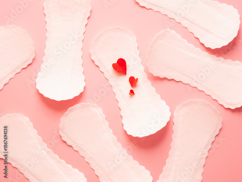 Pattern of white sanitary pads with red paper hearts on pink background menstruation and feminine hygiene concept