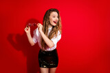 Stylish young woman in elegant attire holding glasses, smiling against a vibrant red background, radiating charm