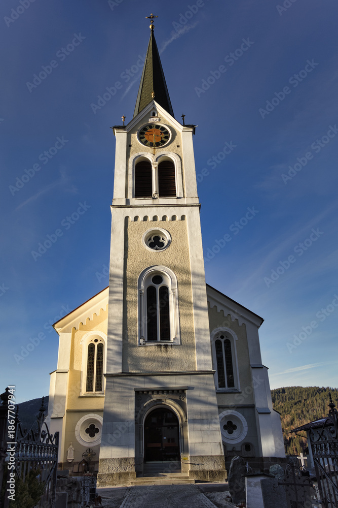 Fototapeta premium Eine helle Kirche mit hohem Turm steht vor blauem Himmel.