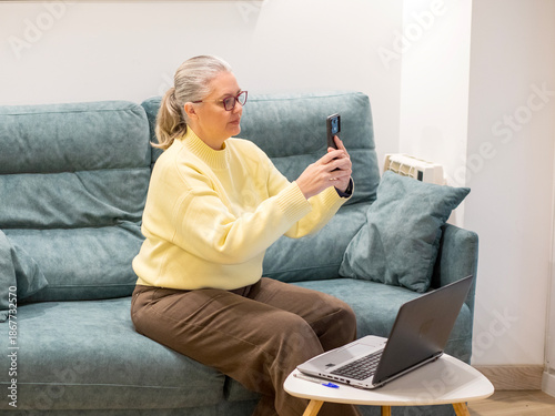 Elderly woman engaged in video call while sitting comfortably at home in cozy sweater
