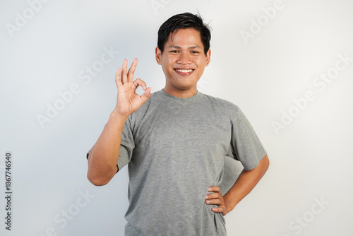 A cheerful man in a gray T-shirt shows an OK gesture, radiating friendliness and positivity.
