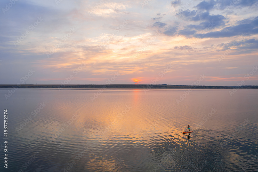 Fototapeta premium Sunset paddleboarder on calm reflective water under colorful sky