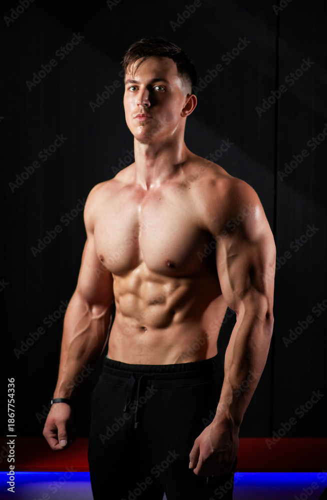 Fototapeta premium Portrait of a sweaty muscular bodybuilder posing on black background.