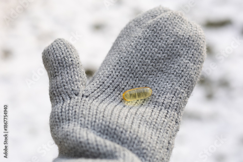Closeup of a person wearing gloves and holding vitamin D capsules. Concept of supplementing vitamin D in winter.