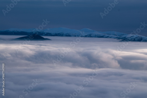 Aerial view of a sea of clouds enveloping the Rakytov mountains, with snow-capped peaks piercing through the misty blanket, Velka Fatra, Zilina Region, Slovakia.
