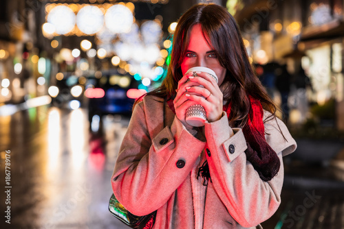 Woman drinking warm coffee on city street at night