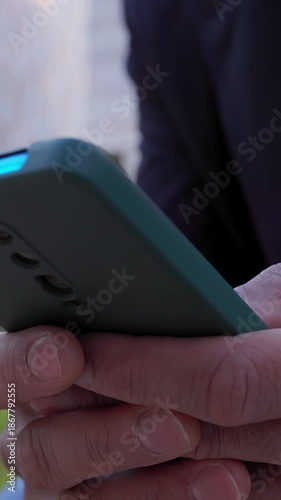 Close-up of adult man using smartphone outdoors. Hands interacting with mobile device during a relaxed moment. Technology and communication concept.