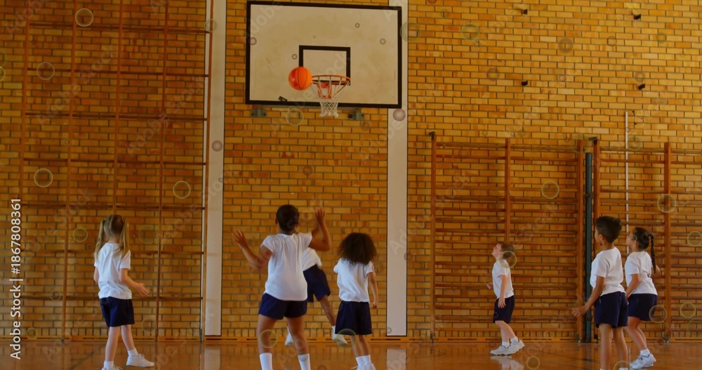 Obraz premium Shooting seven kids in white tees and navy shorts practicing under gym hoop with orange basketball