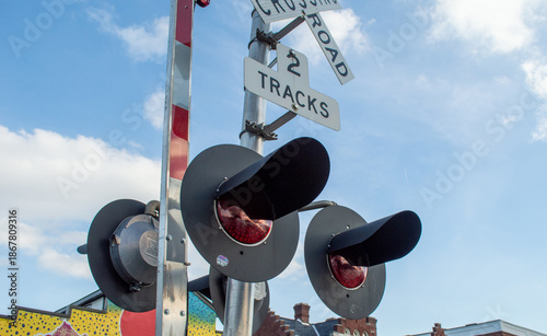 Obraz na plátně Close-up of Railroad Crossing Signal Lights and Signs Against a Bright Blue Sky with Soft Clouds, Warning Drivers and Pedestrians of Approaching Trains at a Level Crossing Intersection