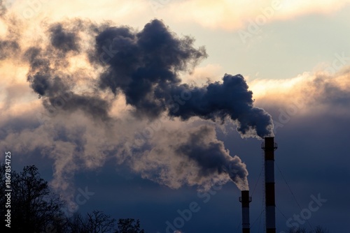 Dark, dense smoke billows from tall industrial chimneys against a dramatic, colorful winter sky, highlighting air pollution and energy production