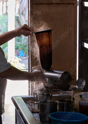 Hot coffee being poured through a cloth filter using the traditional Nanyang brewing method in a kopitiam.