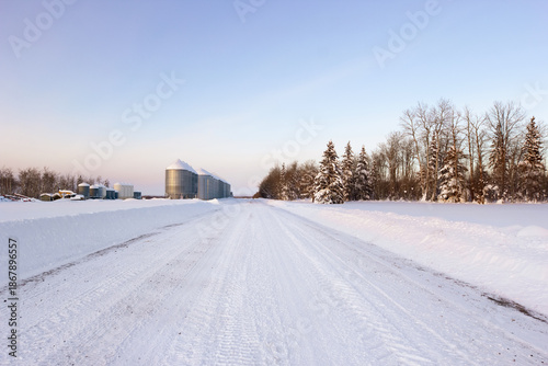 Schilderij op canvas Plowed country road at the farm with granaries in winter.
