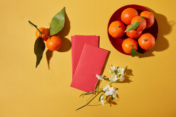 Lunar New Year flat lay scene with red envelopes, lucky fruits and floral accents on yellow background. Clean layout for branding, banners and product mockups