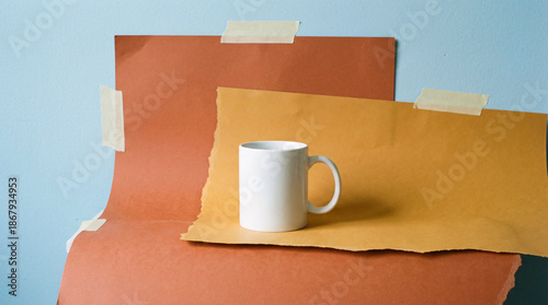 A plain white ceramic mug sits on a yellow-orange paper backdrop, creating a simple studio still life.
