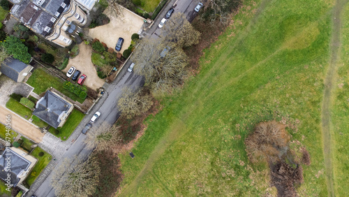 Top-down aerial view of Bath showing Georgian houses and gardens along a quiet street bordering open parkland, with worn footpaths across grass and leafless winter trees.