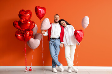 Young couple with heart-shaped balloons near orange wall. Valentine's Day celebration