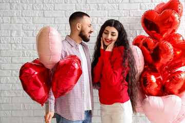 Young couple with heart-shaped balloons on white brick background. Valentine's Day celebration