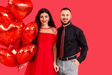 Young couple with heart-shaped balloons on red background. Valentine's Day celebration