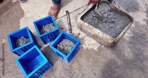 close up of a worker scooping wet concrete into blue plastic cube molds for compressive strength testing.