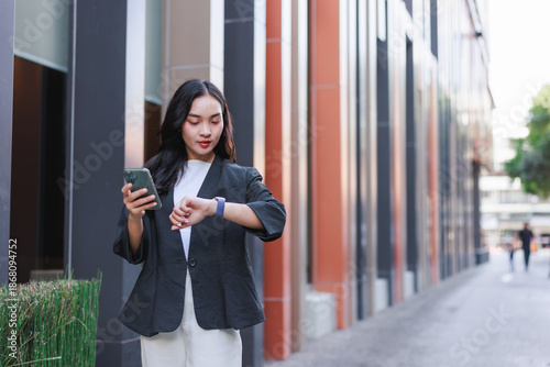 Young businesswoman checking smartwatch and using smartphone in city