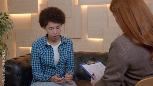 Portrait of anxious uncertain African American woman in life crisis counselling with middle aged female psychotherapist, receiving professional help and consultation to overcome mental problems.