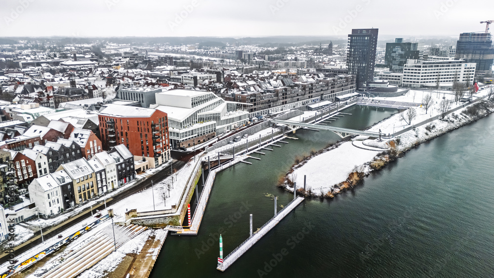 Fototapeta premium Snowy Venlo town waterfront near Maas river aerial drone view, winter cityscape with rooftops covered with snow, winter weather in Limburg, the Netherlands