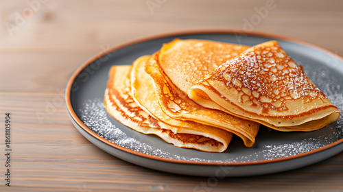 Delicious golden crepes dusted with powdered sugar on a dark plate