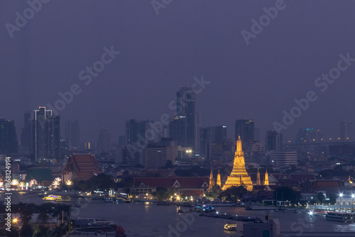 Photography Golden illuminated temple skyline at dusk with river foreground and city tower background