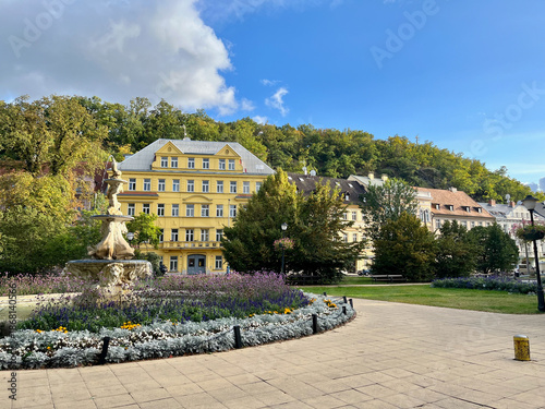 Old fountain in Teplice, Czech Republic, view of historic buildings. Flower bed with flowers. Summer