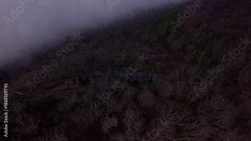 Aerial drone footage of the Brasov sign on Tampa Mountain in Brasov, Romania, with winter haze and forested slopes above the city during daylight in December.