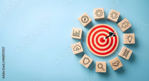 business strategy and goal achievement concept with dart hitting center of bulls eye target surrounded by wooden blocks with corporate icons on blue background for success plan