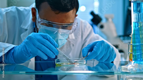 A scientist in a lab coat and protective gear carefully examines a sample in a petri dish. The well-equipped lab, with microscopes and test tubes, highlights precision and focus crucial.