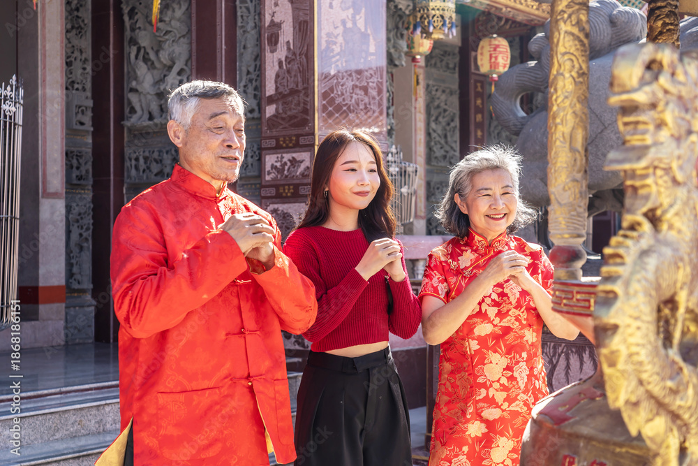 Naklejka premium An Asian family father mother and young daughter dressed in bright cheongsams stands together, hands clasped in prayer, in a vibrant Chinese temple during Lunar New Year celebrations