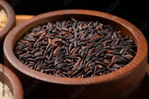 Purple Riceberry rice grains in a brown wooden bowl on black background