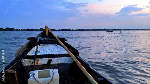 Traditional wooden boat floating on calm water at dusk with serene sky and peaceful horizon