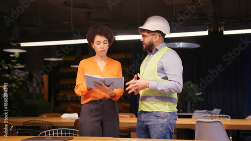Male project manager discussing building plan with female engineer in hard hat and safety vest