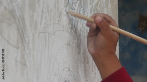 a small boy's hand is drawing or scribbling on a white wall using a simple wooden pencil