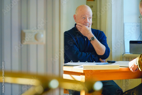 Confident thoughtful conversation with an older man listening attentively to companion at table indoors, hand on chin gesture and calm focus reflecting mindful aging and balanced life after 60.