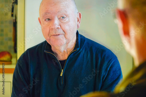 Quality mature lifestyle of older man talking to friend indoors, calm attentive expression and everyday social interaction reflecting mindful aging and life balance.