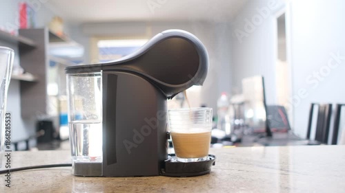 Capsule coffee machine brewing fresh espresso into a glass cup on a kitchen countertop in a modern interior.