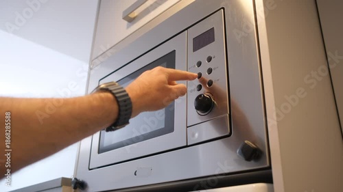 Close-up of a hand operating a stainless steel microwave with digital controls for heating food at home.