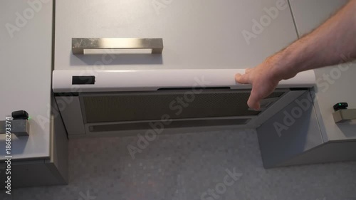 Close-up of a person lifting a stove extractor hood to turn on ventilation and lights in a contemporary kitchen.